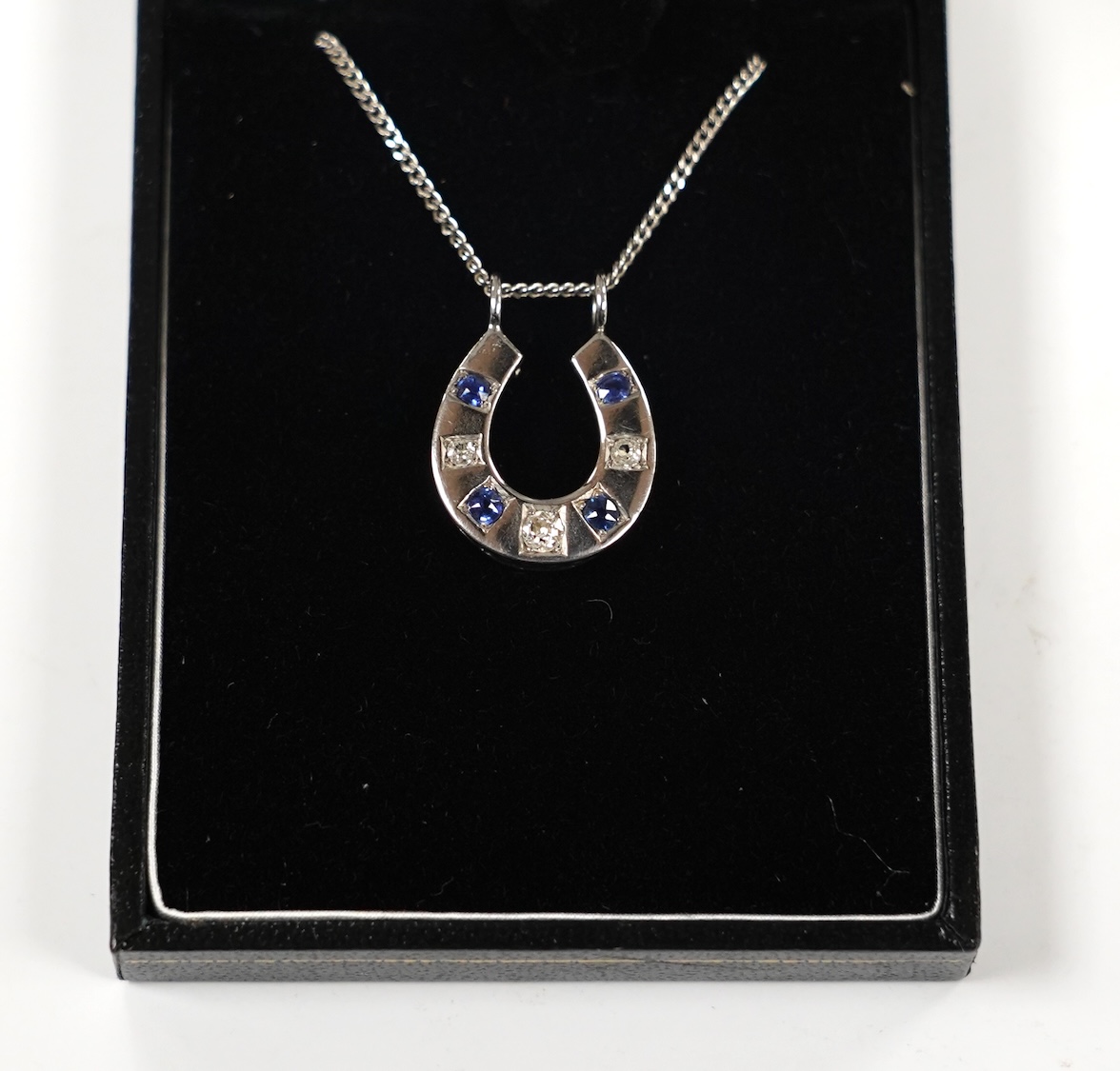 A modern 18ct white gold, sapphire and diamond set horseshoe pendant on chain, overall 44cm, gross weight 5.5 grams.